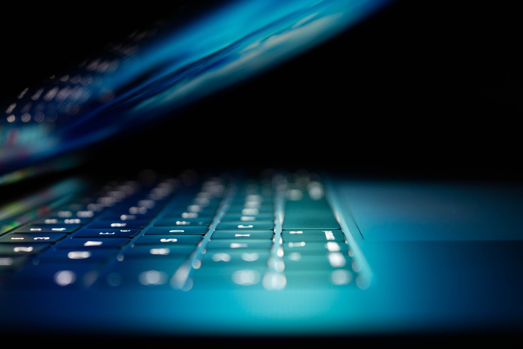 Close up of a laptop keyboard lit by the screen tilted above it