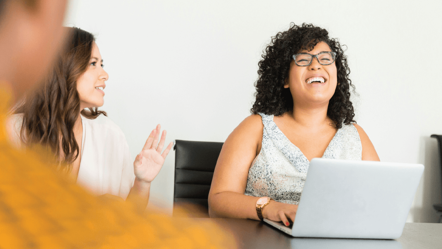 Smiling woman on a laptop at a meeting table with two other people.